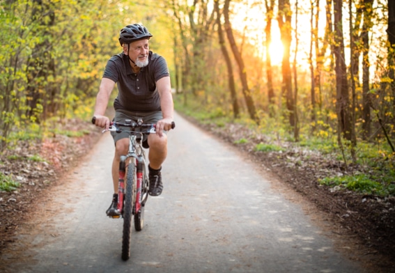 Senior man riding bicycle down a path in the woods.