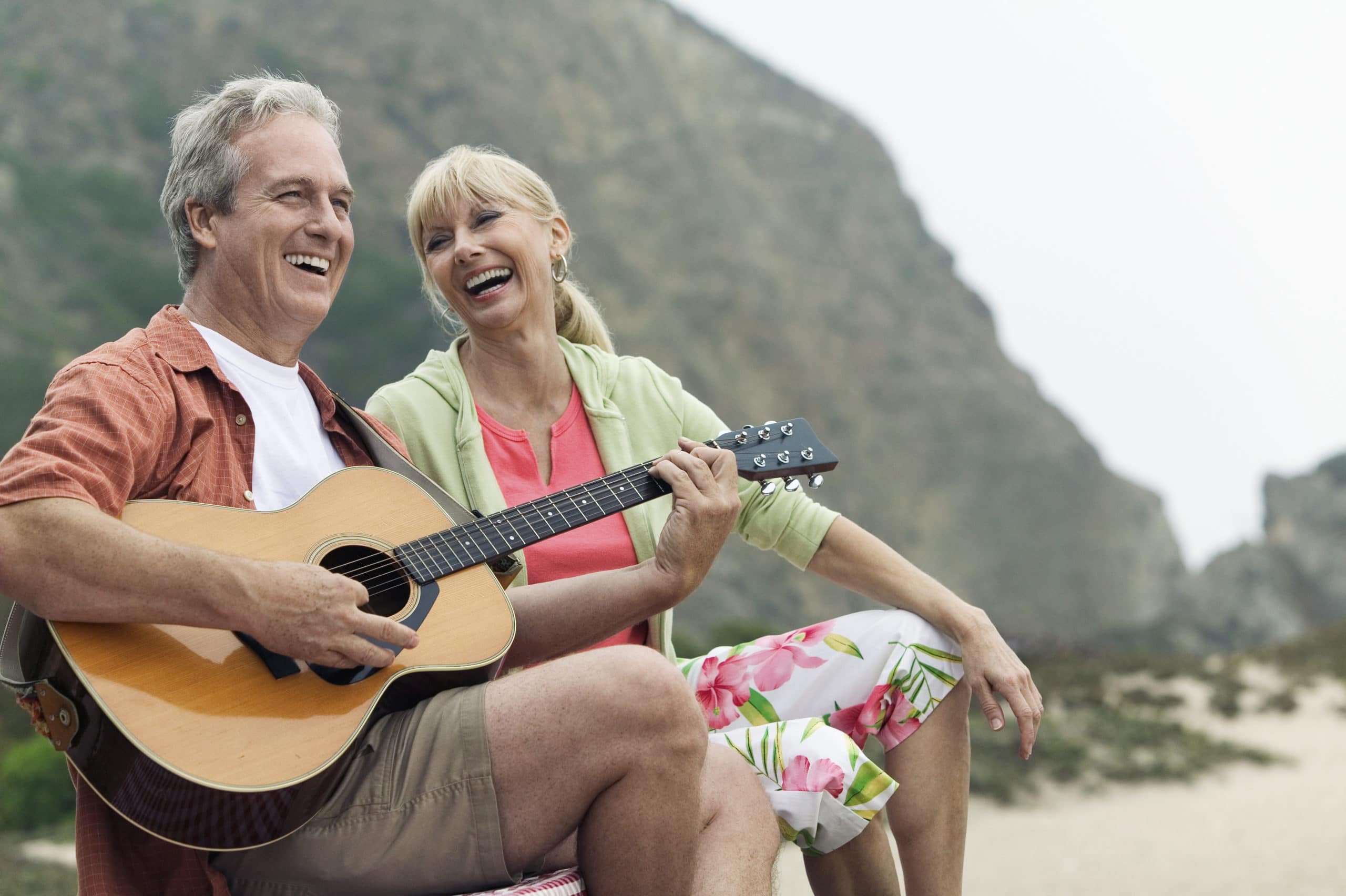 Happy senior couple playing guitar on the beach